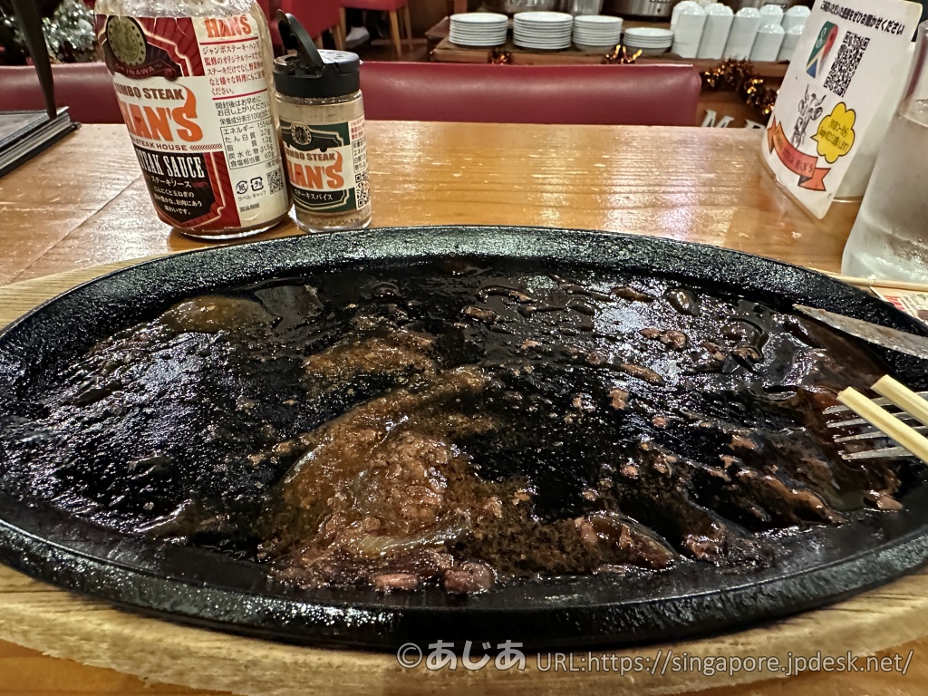 ステーキを食べ終え、肉汁とソースの跡だけが残った空の黒い鉄板。奥には調味料のボトルが置かれている。
