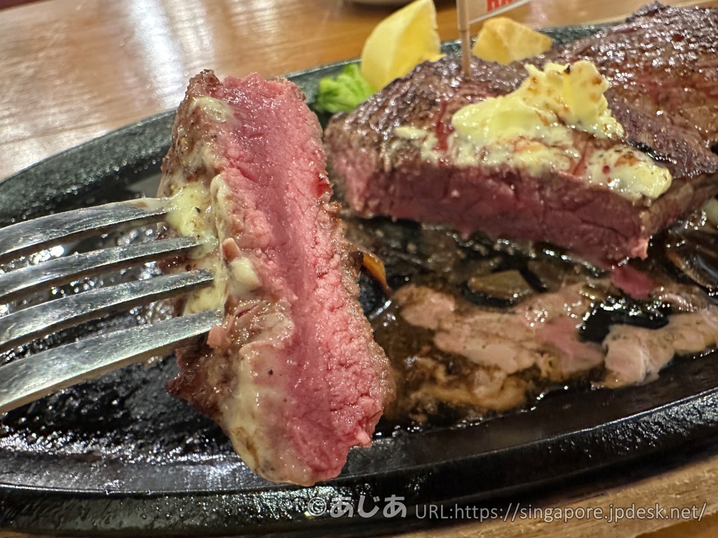 フォークで持ち上げられたランプステーキの断面アップ。中は美しいピンク色（ミディアムレア）で、外側はこんがりと焼け、溶けたバターが乗っている。