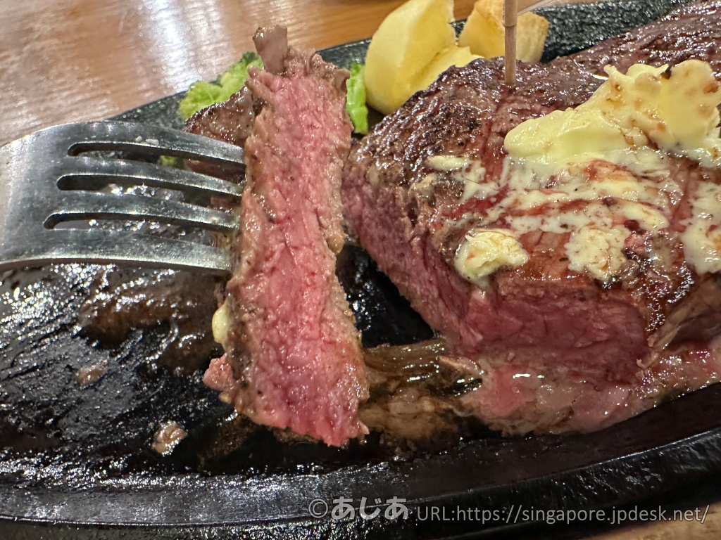 フォークに刺さった分厚いカットステーキのアップ。赤身の肉質がしっかりしており、ジューシーな肉汁が光っている。