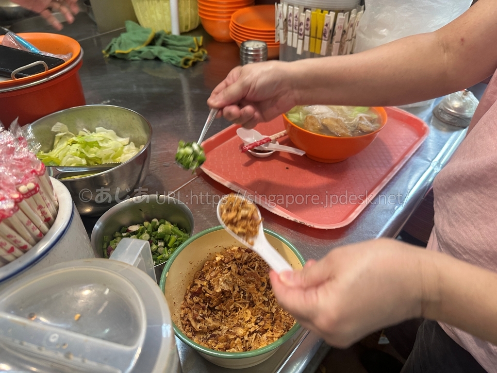 Kwang Keeの店員がフライドオニオンを丼にのせる様子