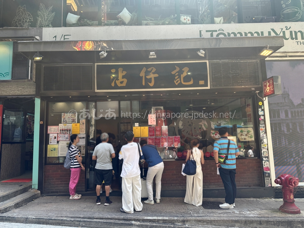 香港中環のワンタン麺店・沾仔記の黒と金の看板と店頭の行列