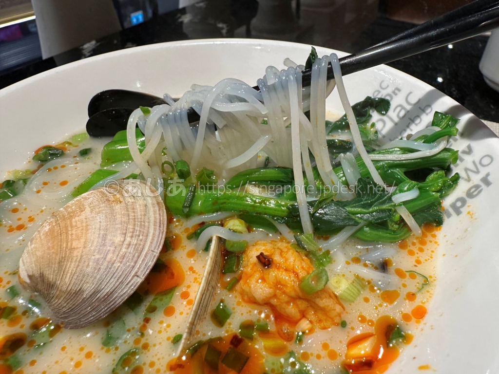 スポットライトの海鮮麺の透明麺、貝、エビ、青菜のアップ