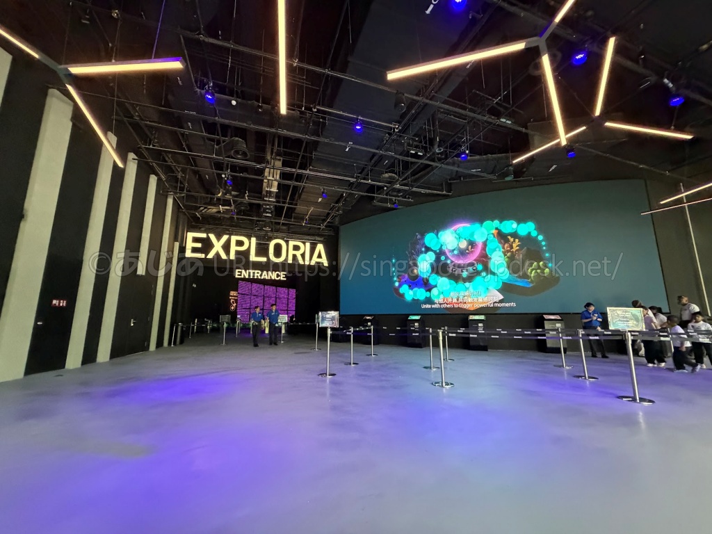 Exploriaのエントランスホールの大型スクリーンの前にあるキオスクと入場ゲートの上のExploriaのサイン