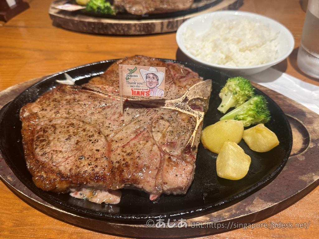 黒い鉄板に乗った大きなTボーンステーキ。横にはライス、ブロッコリー、じゃがいもが添えられている。